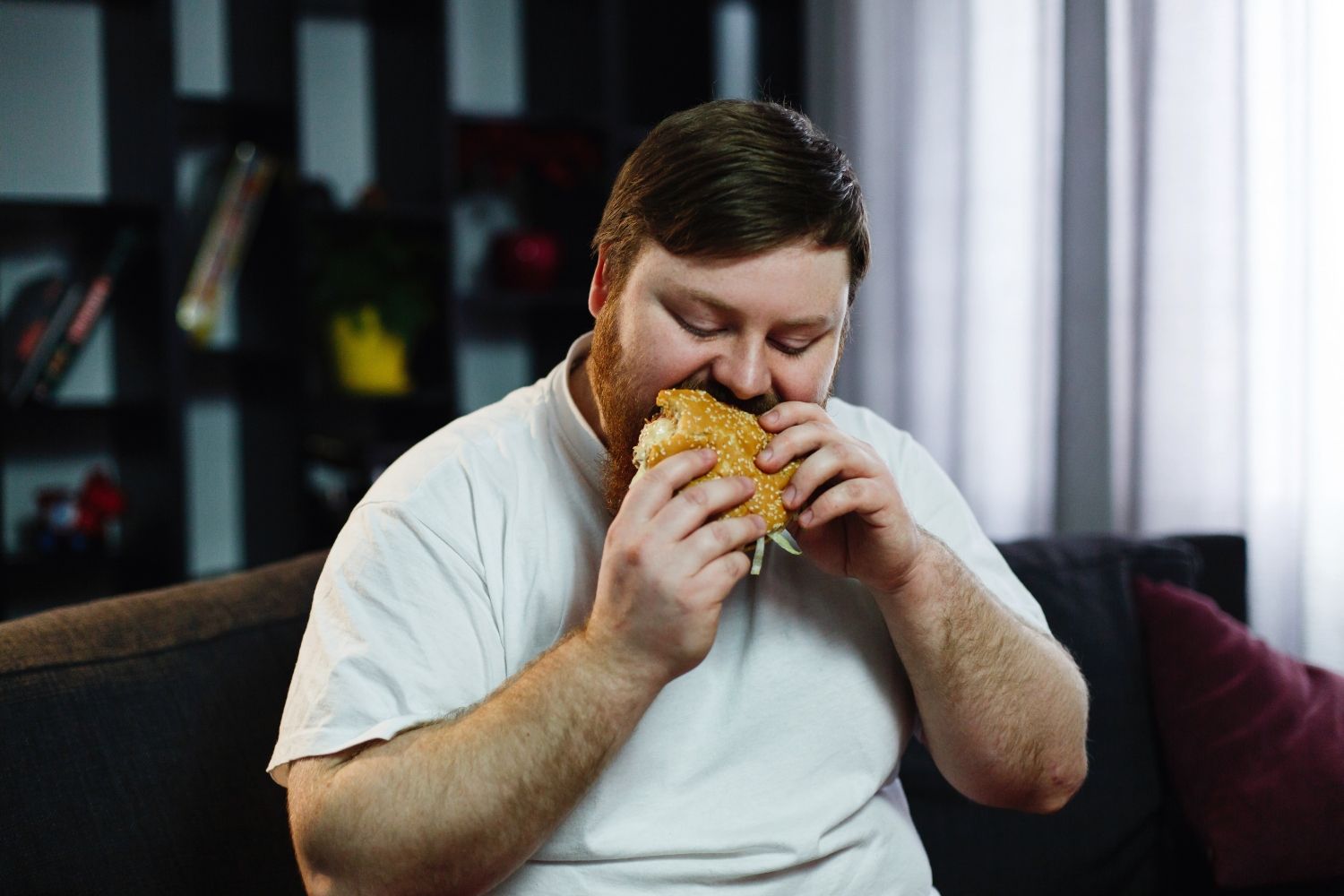 Un hombre con sobrepeso devora una hamburguesa / FREEPIK