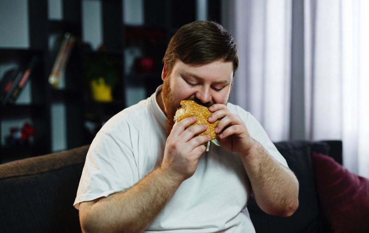 Un hombre con sobrepeso devora una hamburguesa / FREEPIK