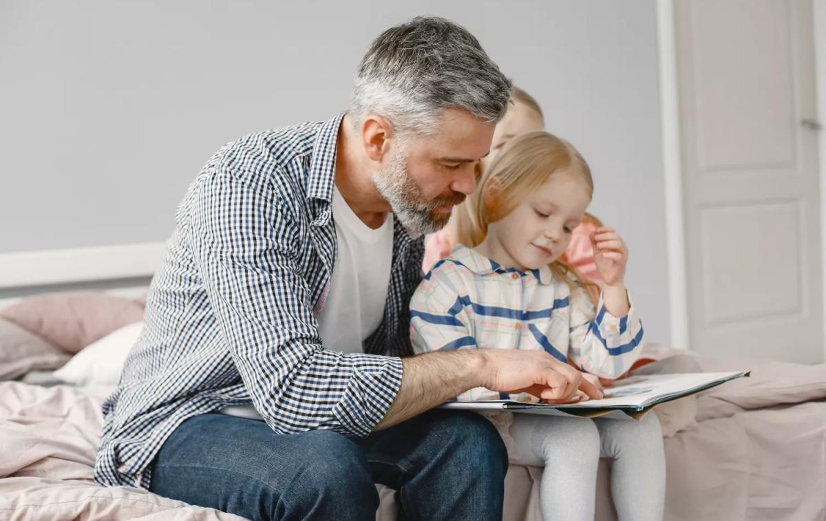 Un padre lee a su hija un cuento / FREEPIK