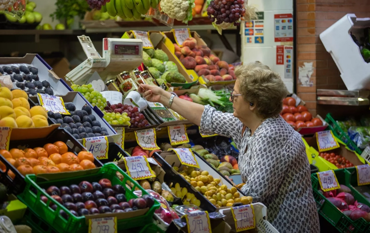 Una mujer compra en uno de los puestos del mercado de abastos de Triana (Sevilla) y comprueba la subida de los alimentos / MARÍA JOSÉ LÓPEZ (EP)