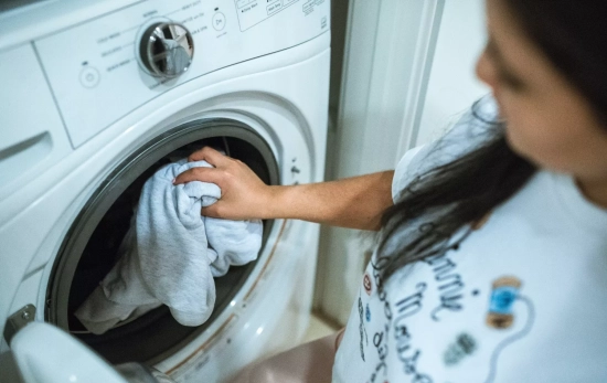 Una mujer pone la lavadora después de dejar su prenda en remojo/ PEXELS