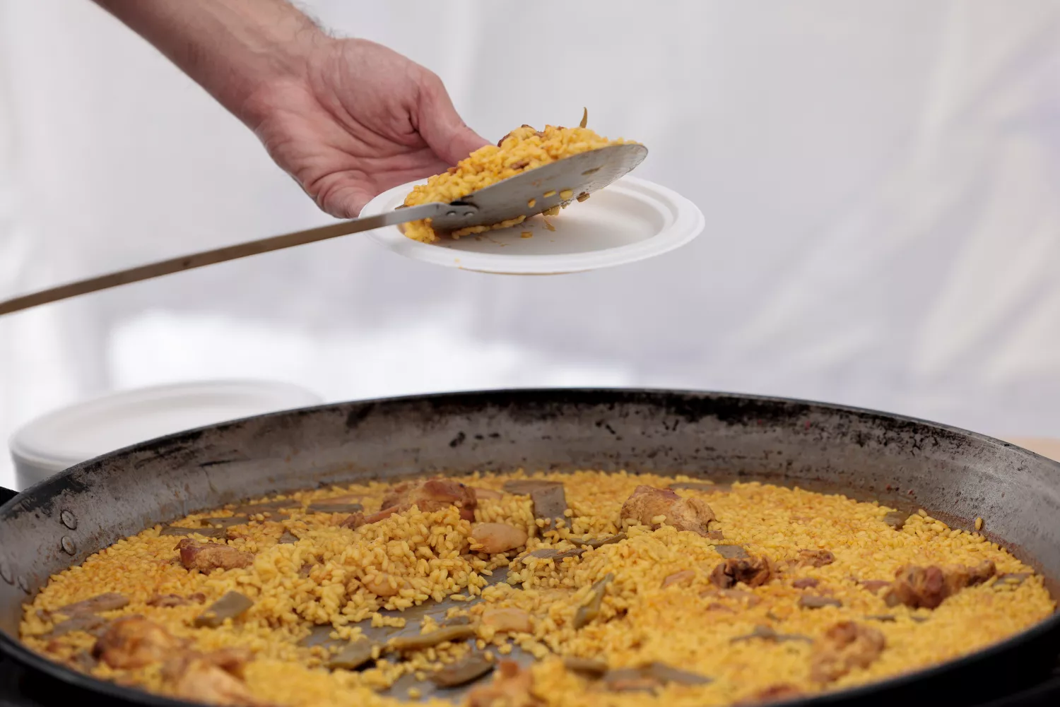 Una persona sirve un plato durante el  World Paella Day, que ha ganado un chef japonés / EFE - ANA ESCOBAR