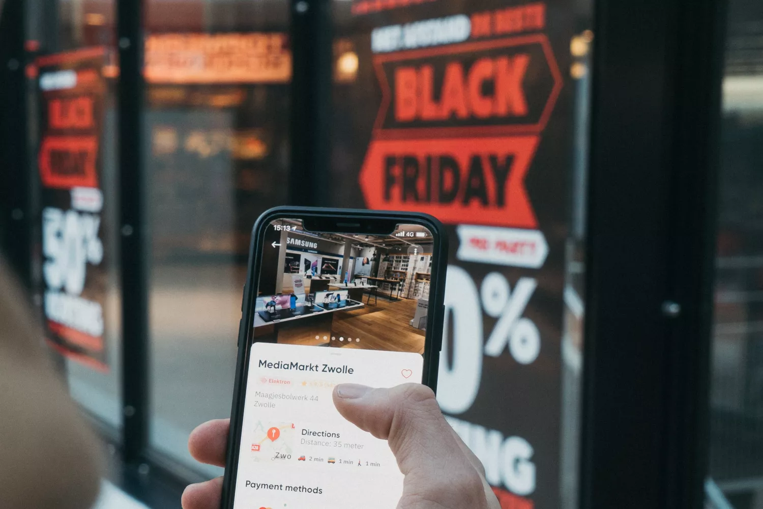 Una persona mira su móvil delante de un cartel que anuncia ofertas por Black Friday / UNSPLASH