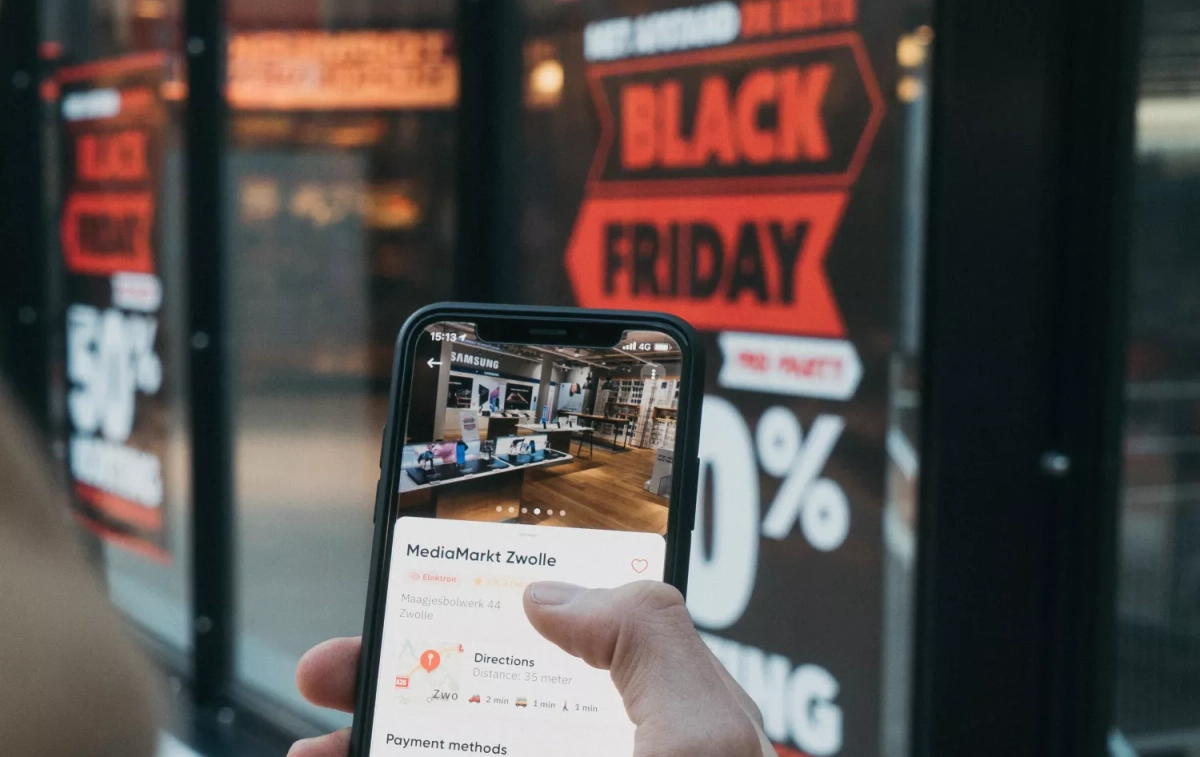 Una persona mira su móvil delante de un cartel que anuncia ofertas por Black Friday / UNSPLASH