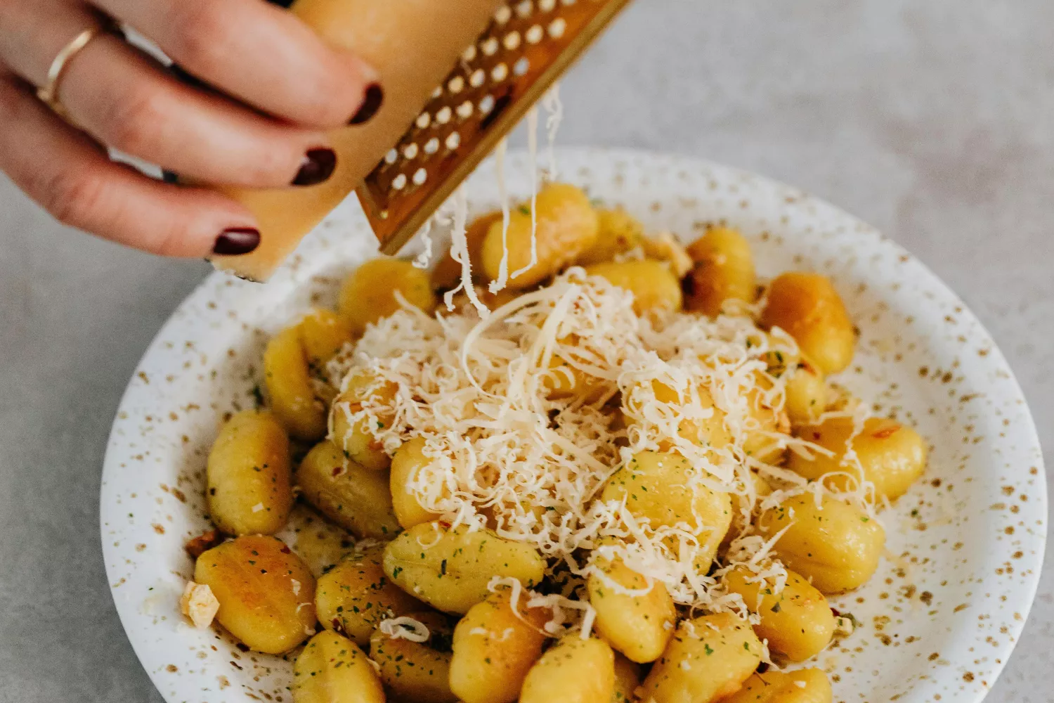 Una persona ralla queso sobre un plato de ñoquis / PEXELS