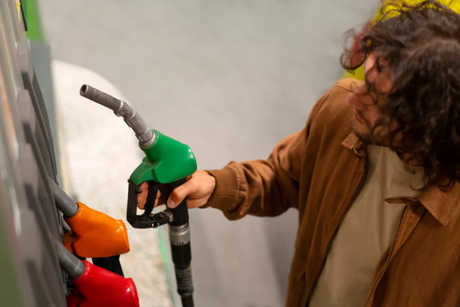 Un hombre sostiene una manguera para llenar el depósito de su coche de gasolina / FREEPIK
