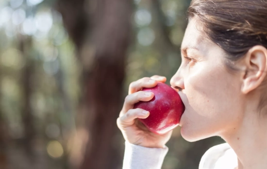 Una persona muerde una manzana, uno de los alimentos que ayudan a mantener un corazón sano / FREEPIK