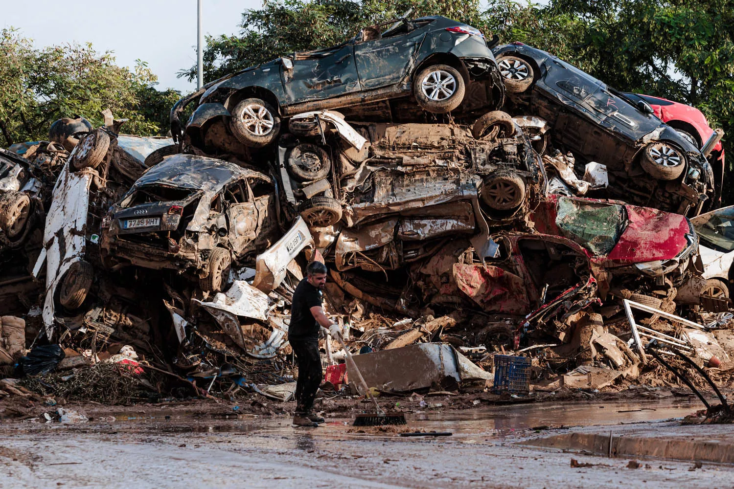 Una persona limpia entre coches amontonados en Alfafar tras el paso de la DANA / CARLOS LUJÁN - EUROPA PRESS