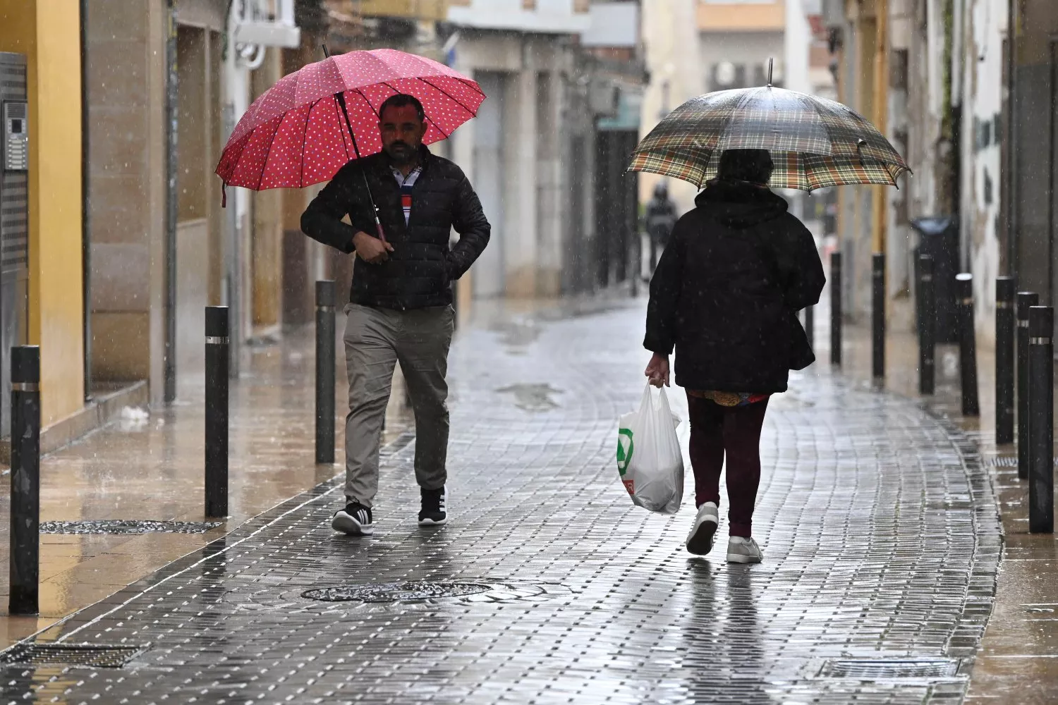 Unos viandantes se protegen de la lluvia este jueves y luego pondrán la calefacción en casa / Andreu Esteban - EFE