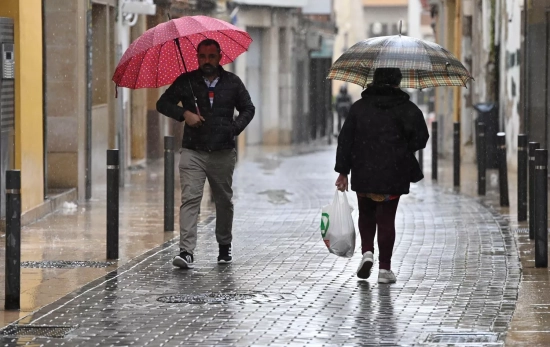 Unos viandantes se protegen de la lluvia este jueves y luego pondrán la calefacción en casa / Andreu Esteban - EFE