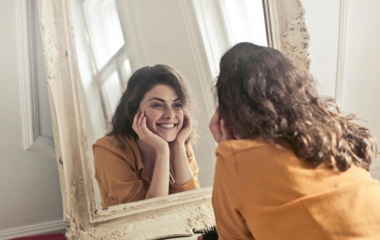 Una mujer que se siente feliz y plena se mira al espejo/ PEXELS