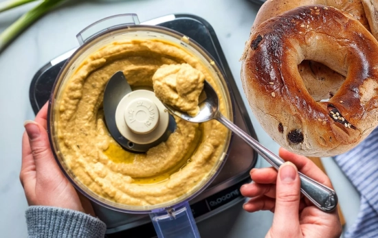 Una persona rellena un bagel de hummus/ Montaje Consumidor Global Una persona rellena un bagel de hummus/ Montaje Consumidor Global
